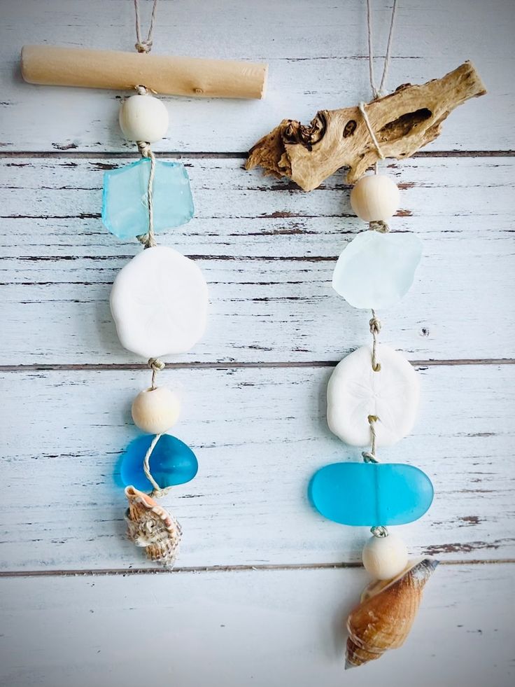 sea glass and seashells are hanging on a white wooden background with a piece of driftwood