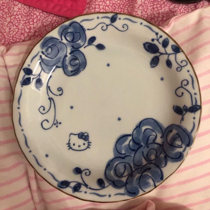 a hello kitty plate sitting on top of a pink and white striped bed sheet with a black cat in the center