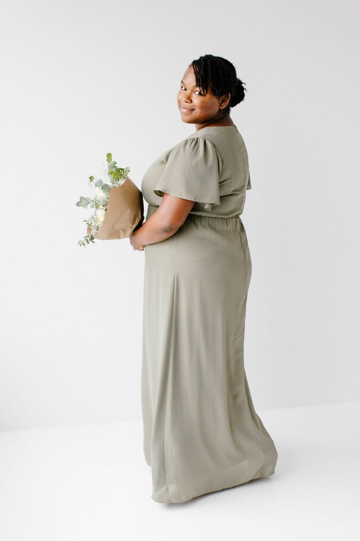 a woman holding a bouquet of flowers in her hand and smiling at the camera while standing against a white background