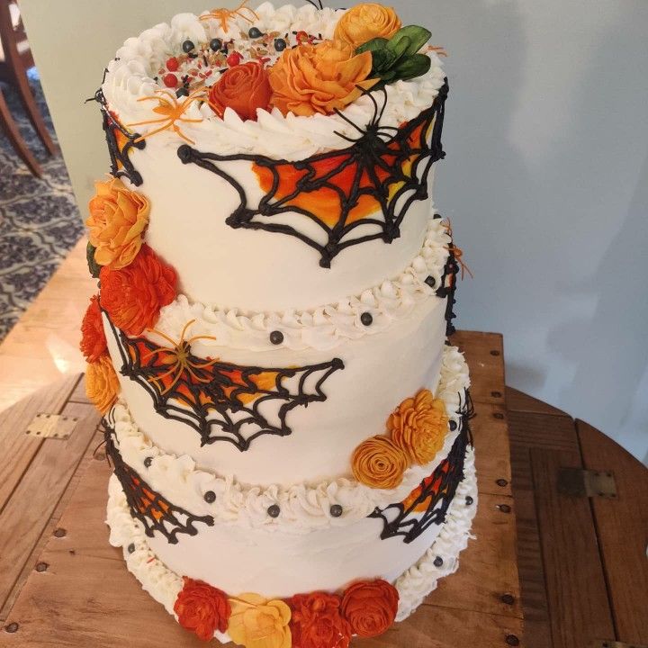 a three tiered cake decorated with orange flowers and spider webs on the side