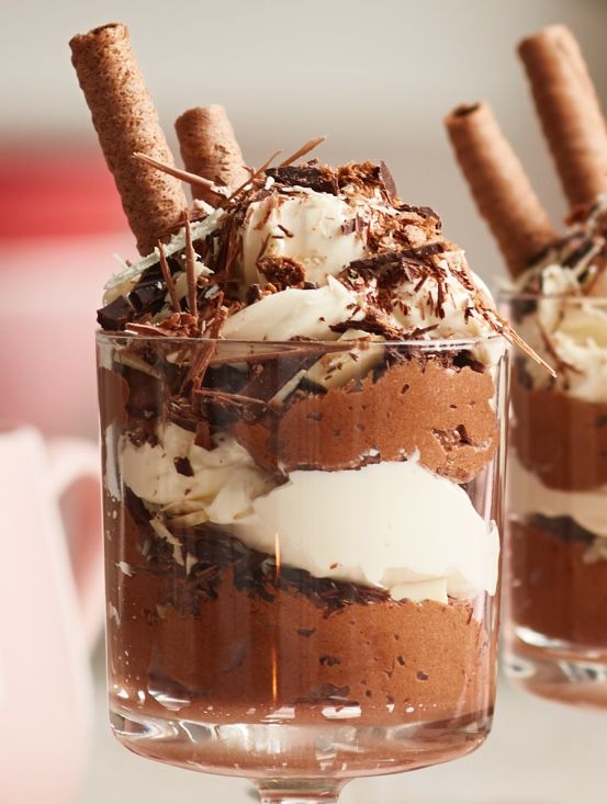 two desserts with chocolate and whipped cream in glass dishes on a white table top