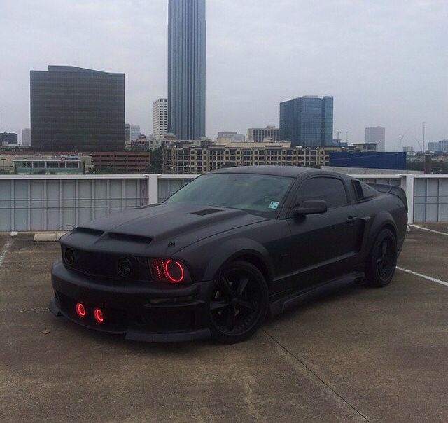 a black sports car parked in a parking lot next to tall buildings and skyscrapers