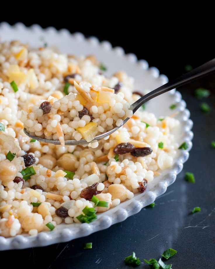 a white bowl filled with rice and topped with chopped green onions next to a spoon