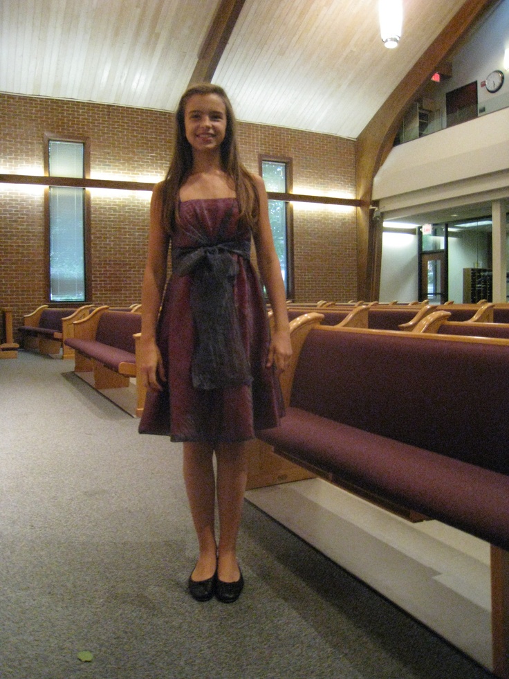 a woman standing in front of a row of pews wearing a purple dress and black shoes