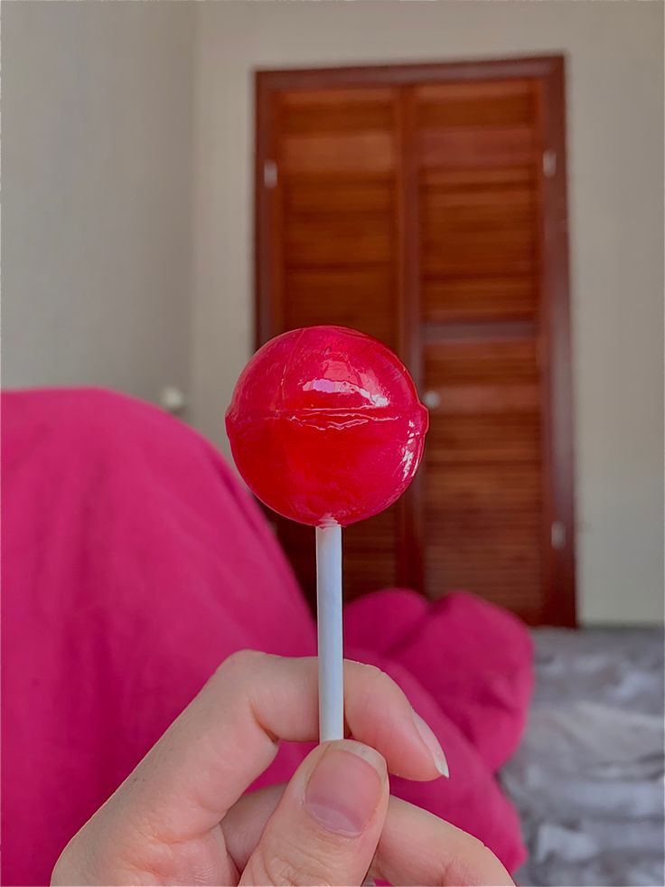 a person is holding a red lollipop in their hand and it looks like they are eating something