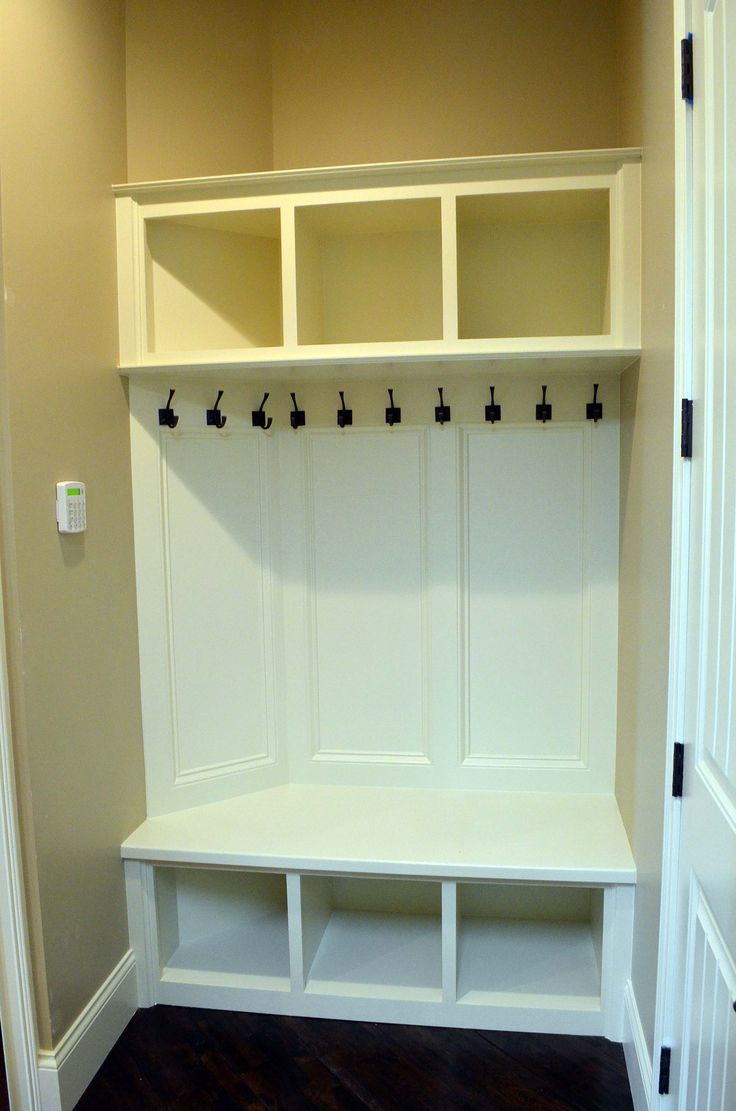 an empty white mud room with built - in shelves and hooks on the door knobs