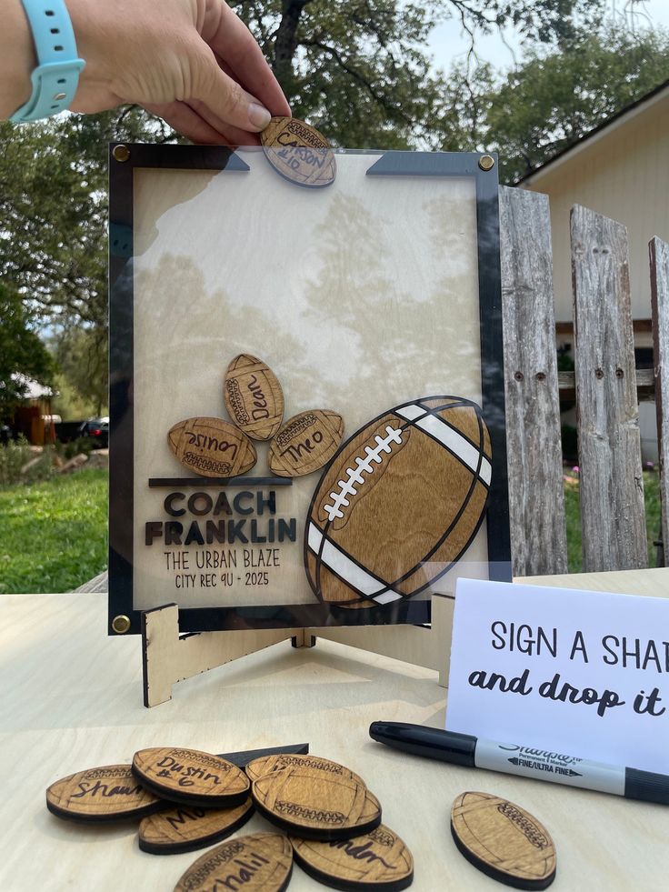 a hand is holding a football and some other items on a table with a sign that says, sign a shape and drops it