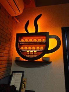 there is a coffee cup on the wall with lights above it and an illuminated shelf below