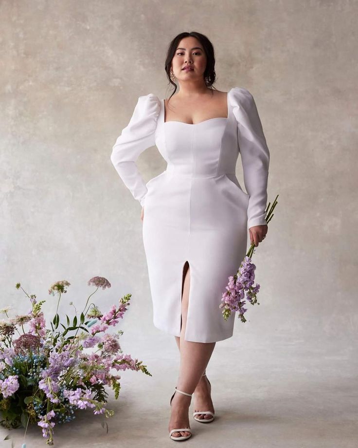 a woman in a white dress standing next to flowers