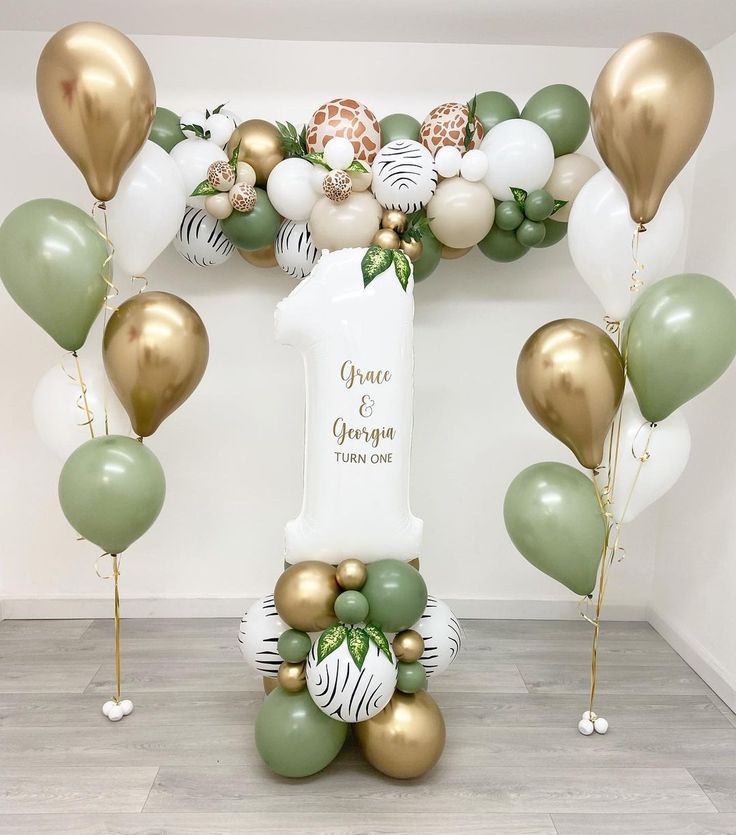 an arch made out of balloons and greenery is decorated with gold, white, and green balloons