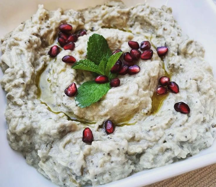 hummus with pomegranates and mint on top in a white bowl