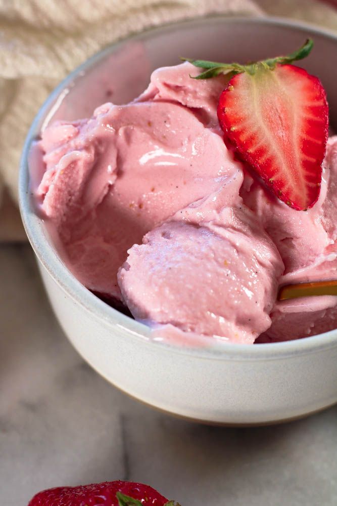 a bowl filled with ice cream next to a strawberry