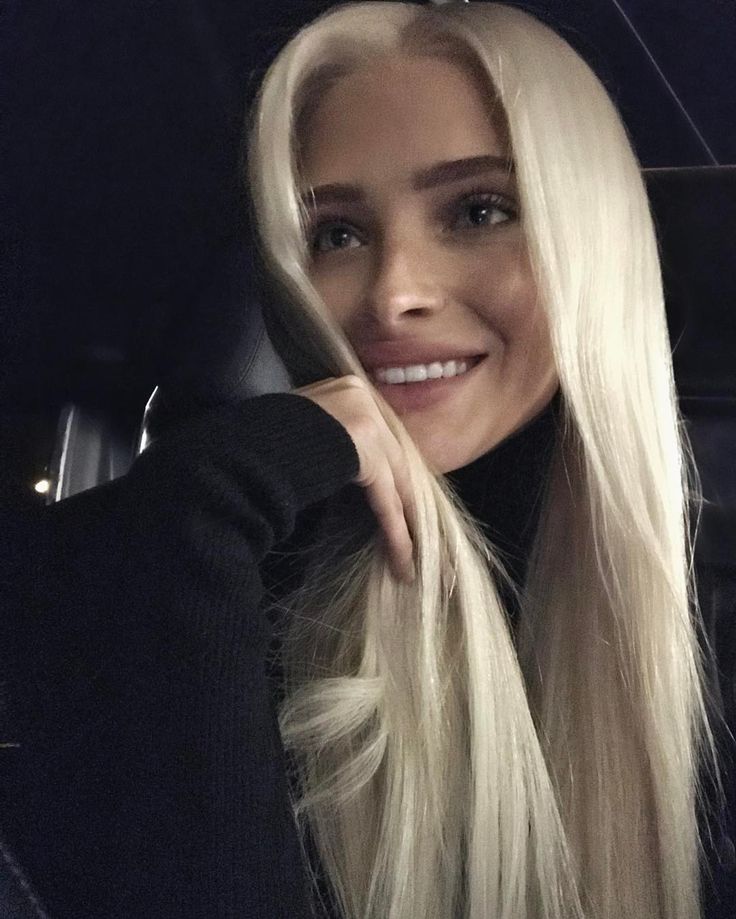 a woman with long blonde hair sitting in the back seat of a car smiling at the camera