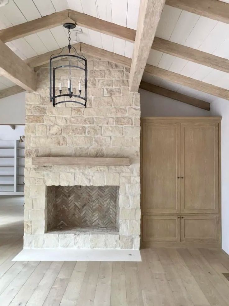 an empty living room with wood floors and stone fireplace in the center, surrounded by wooden beams