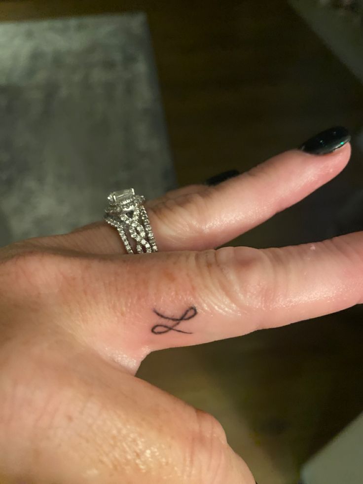 a person's hand with a ring on it and a cross tattoo on the middle finger