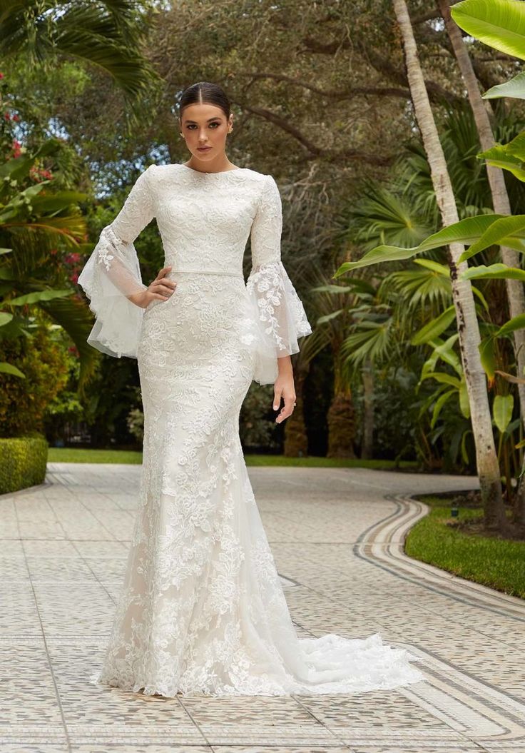 a woman in a white wedding dress standing on a brick walkway with palm trees behind her