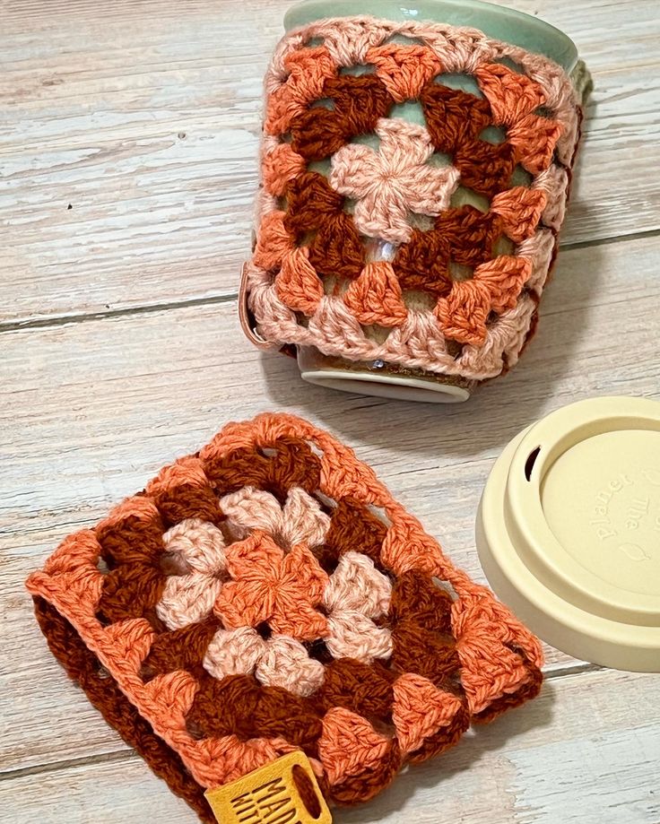 two crocheted coasters sitting on top of a wooden table next to a coffee cup