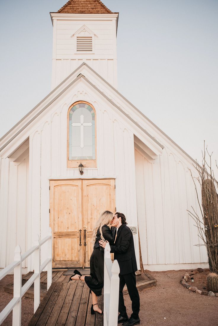 a man and woman kissing in front of a white building with a cross on it