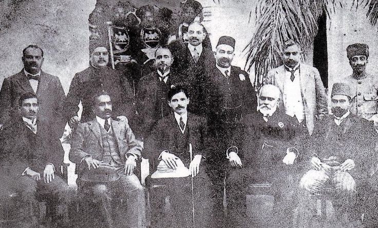 an old black and white photo of men in suits posing for a group shot with palm trees behind them