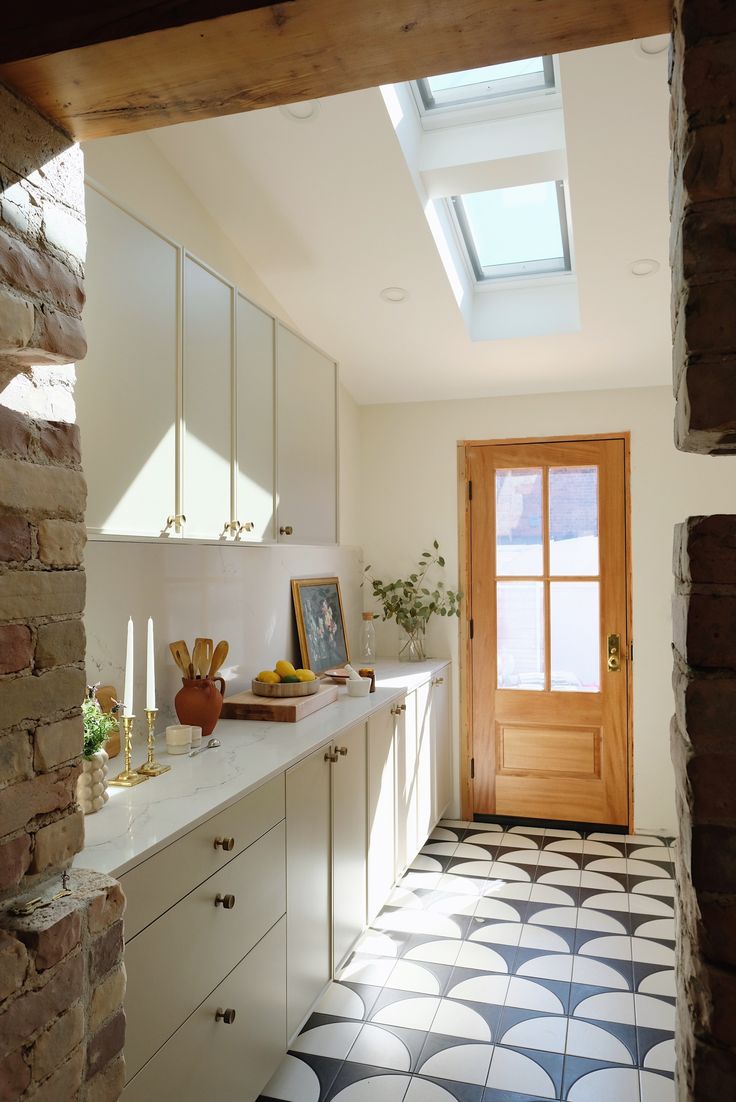 a kitchen with white cabinets and black and white tile flooring next to a wooden door