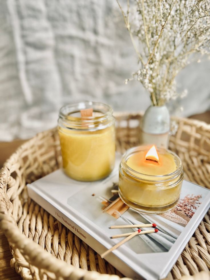 a wicker basket with a candle, book and matches on it next to a vase filled with baby's breath