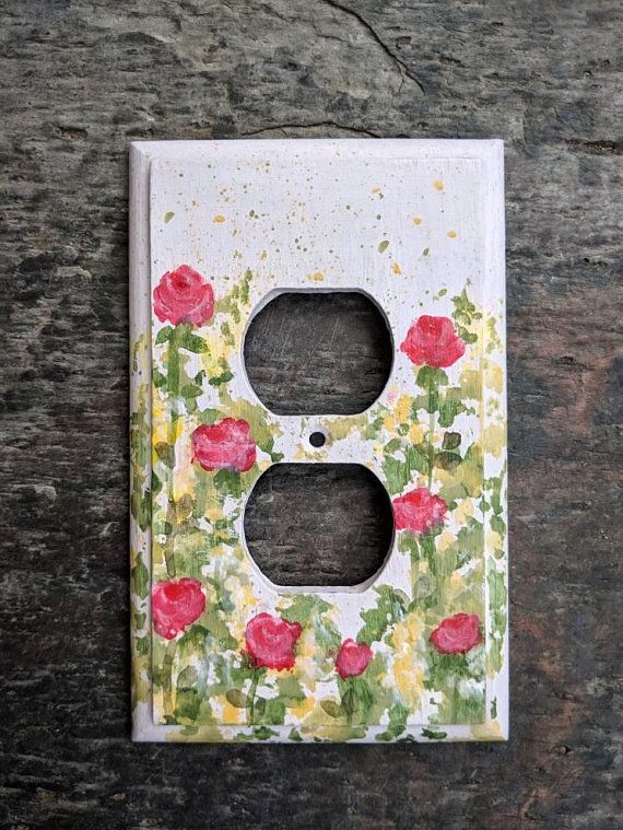 a painted light switch cover on a wooden surface with red and yellow flowers in the center