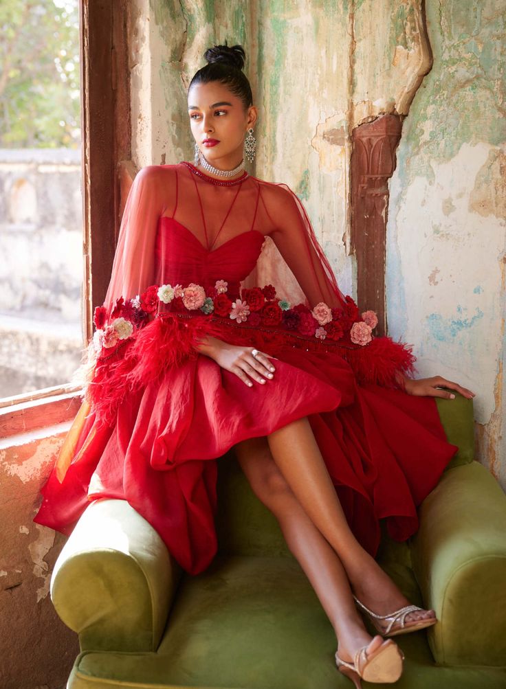 Editor's Note Playful yet chic, featuring a statement handmade floral corsages in a red cape set which includes a draped skirt, paired with a bralette & a flared cape. The cape is embellished with handmade 3D flowers and feathers. Fabric: Mono net, organza Color: Red Component: Cape, bralette and drape skirt Occasion: Cocktail Note: Product colour may slightly vary due to photographic lighting sources Care: Dry Clean Only About the Designer Varun Bahl, a renowned designer, skillfully blends the Elegant Tulle Dresses For Red Carpet, Red Organza Dress For Gala, Organza Cape Dress For Wedding, Red Cape Evening Dress, Red Cape Dress For Party, Red Cape Sleeve Dress For Evening, Spring Party Evening Dress With Cape Sleeves, Glamorous Fitted Cape Dress, Festive Chic Dresses With Cape Sleeves