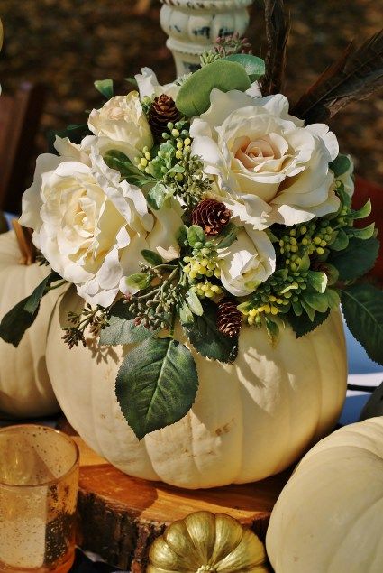 a white pumpkin filled with flowers and greenery on top of a wooden table next to other fall decorations