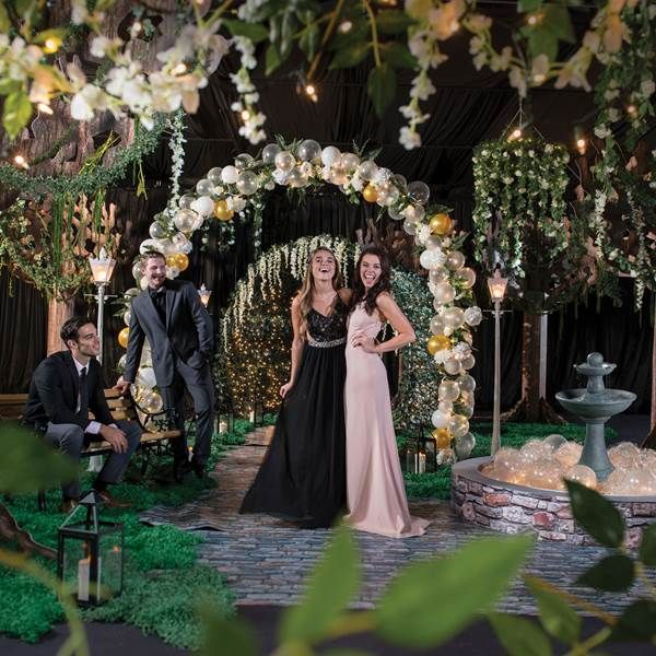 two people standing in front of an archway with flowers and greenery on the ground