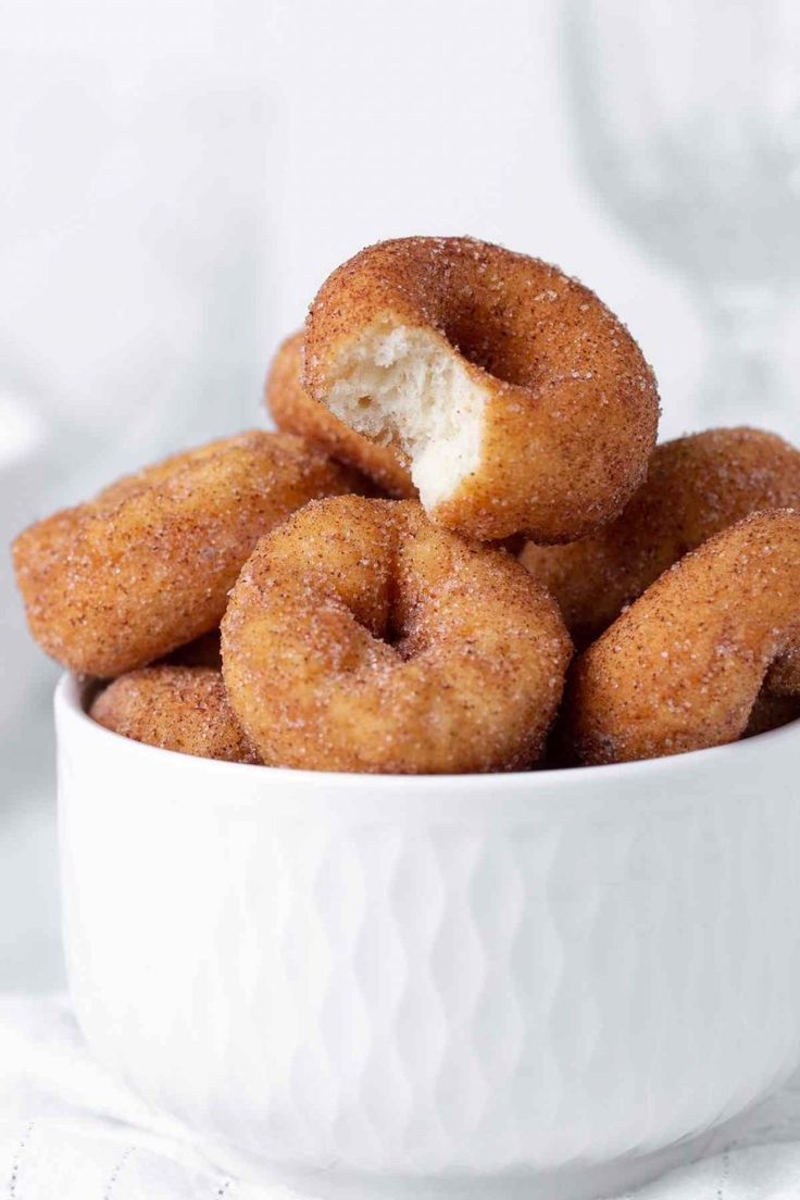 a white bowl filled with sugared doughnuts on top of a cloth covered table