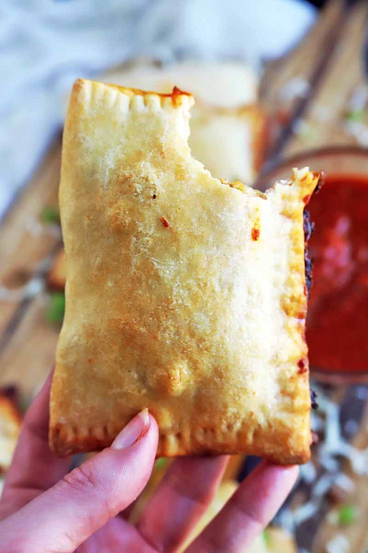 a person holding up a piece of food with sauce in the background