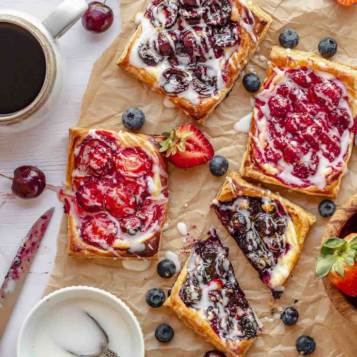 berry cheesecakes with whipped cream and fresh berries on the side, next to a cup of coffee