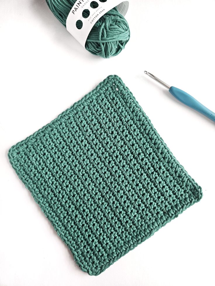 a crochet dishcloth next to a ball of yarn and a knitting needle