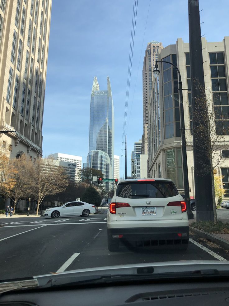 the back end of a white car driving down a street in front of tall buildings