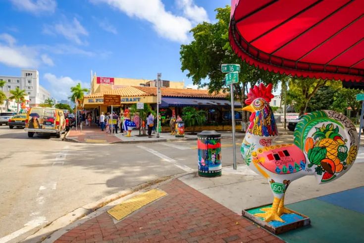 a large rooster statue on the side of a road next to a red awning