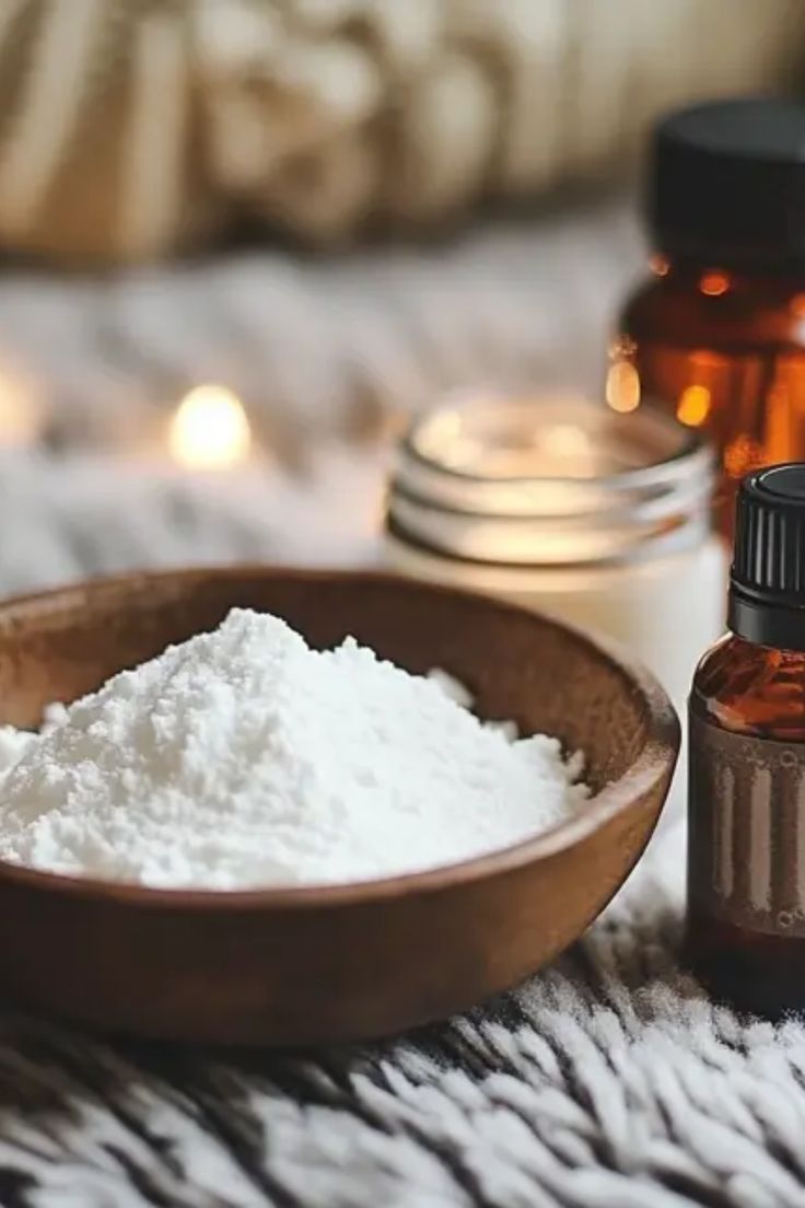 a wooden bowl filled with white powder next to two bottles of essential oils on a bed