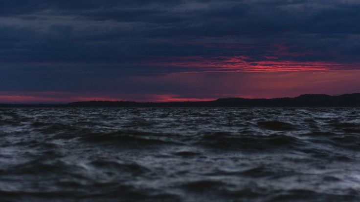 the sun is setting over the ocean with dark clouds