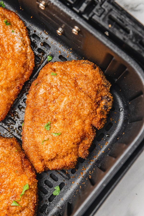 four fried chicken patties in an air fryer with parsley sprinkled on top