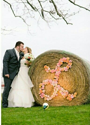 a bride and groom kissing in front of a hay bale with flowers on it