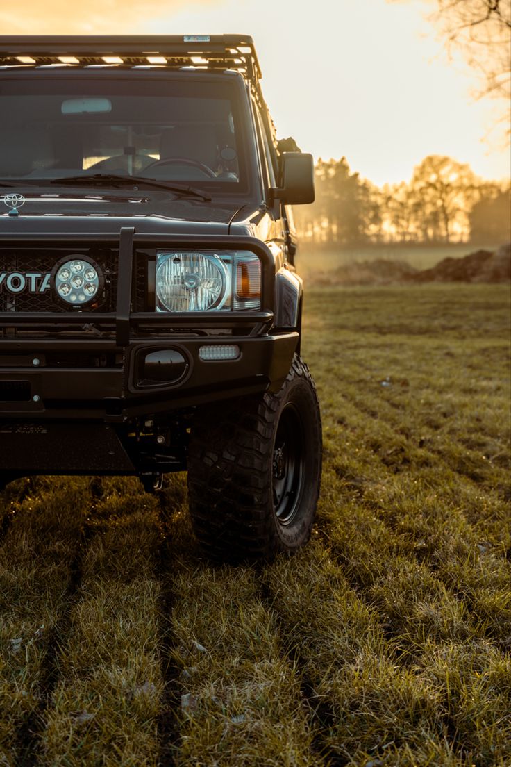 the front end of a four wheel drive vehicle parked in a grassy field at sunset