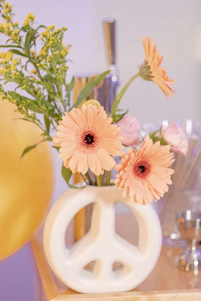 pink flowers in a white vase with peace sign decoration on the table next to it