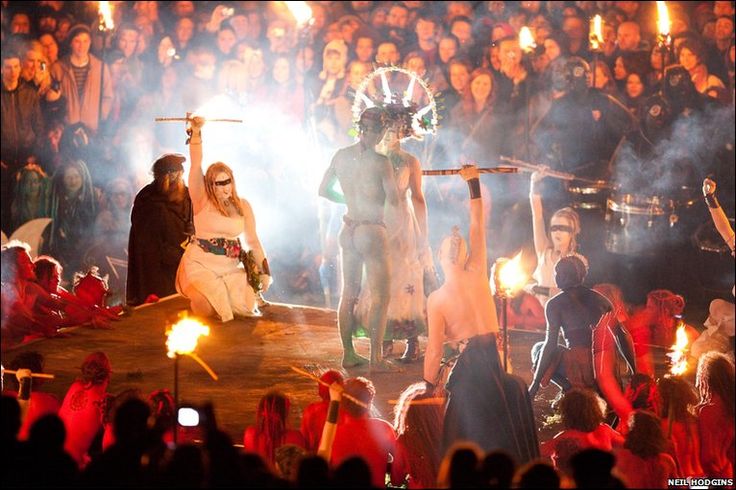 two women dressed in costumes stand on stage with torches as people watch from the audience