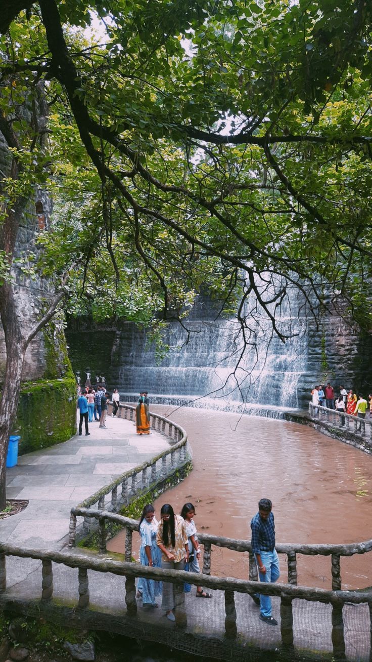 several people are standing on a bridge near a waterfall