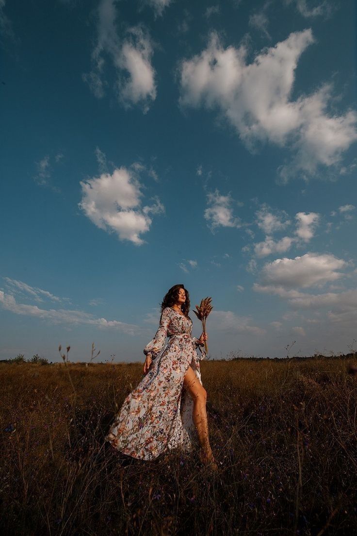 a woman in a long dress is walking through the grass with her legs spread out