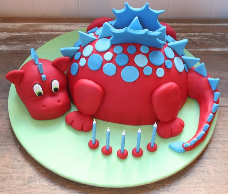 a red cake with blue decorations and candles on a green plate, sitting on a wooden table