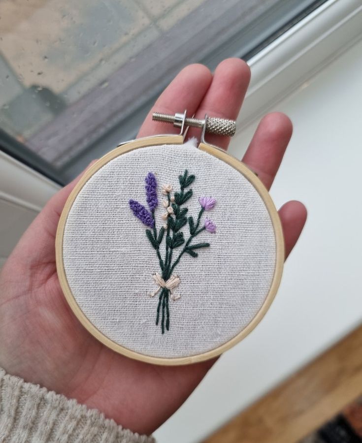 a hand holding a small embroidered flower in front of a window