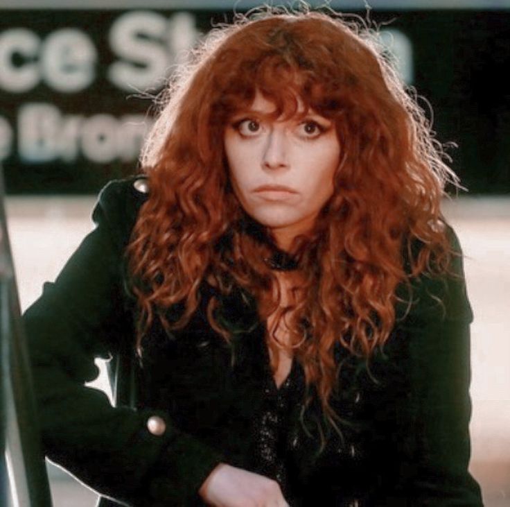 a woman with long red hair standing next to a metal railing and looking at the camera