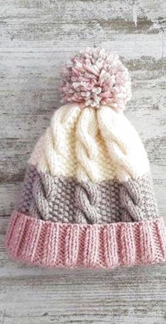 a knitted hat on top of a wooden floor with white and pink yarns