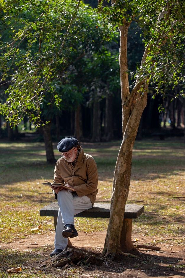 a man sitting on a bench next to a tree and looking at his cell phone