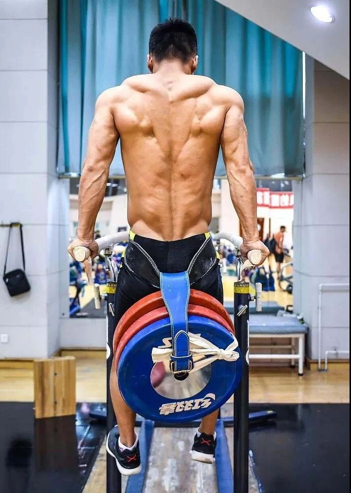 a man with no shirt on standing next to a gym machine and looking at the camera